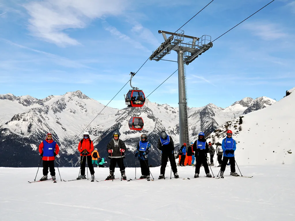 Skigruppe steht unter der Seilbahn vor den Bergen.
